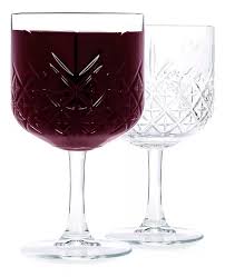 Dos copas de vidrio labrado con diseño facetado, una vacía y la otra con una bebida en su interior.